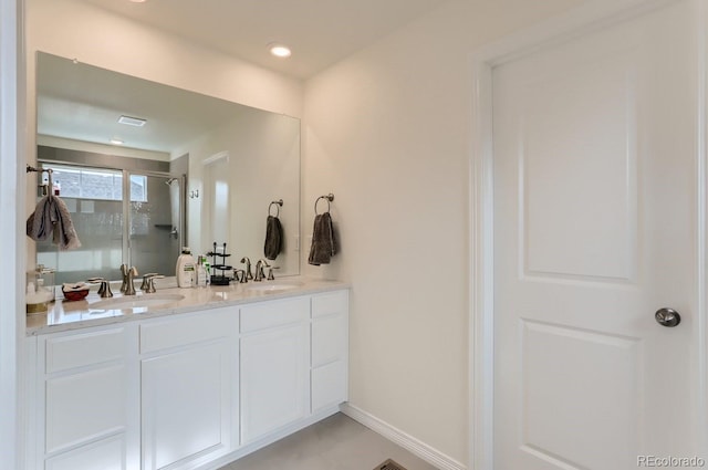 bathroom featuring a sink, double vanity, a stall shower, and baseboards