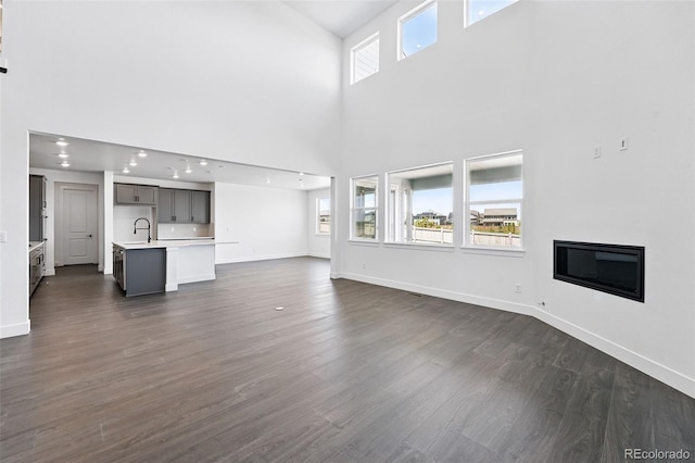 16565 Black Rose Cir, Parker, CO 80134 - unfurnished living room with a high ceiling, a glass covered fireplace, a sink, baseboards, and dark wood-style floors