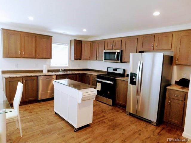 kitchen with sink, light hardwood / wood-style flooring, appliances with stainless steel finishes, and a kitchen island