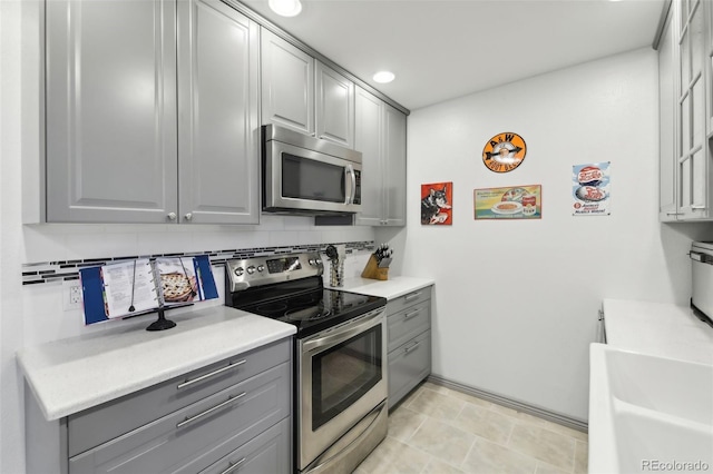 kitchen featuring gray cabinetry, light tile floors, backsplash, and appliances with stainless steel finishes