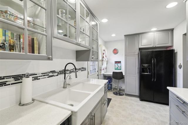 kitchen with tasteful backsplash, light tile flooring, gray cabinets, black refrigerator with ice dispenser, and sink