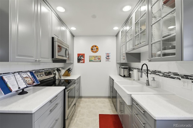 kitchen with backsplash, light tile flooring, gray cabinetry, and stainless steel appliances