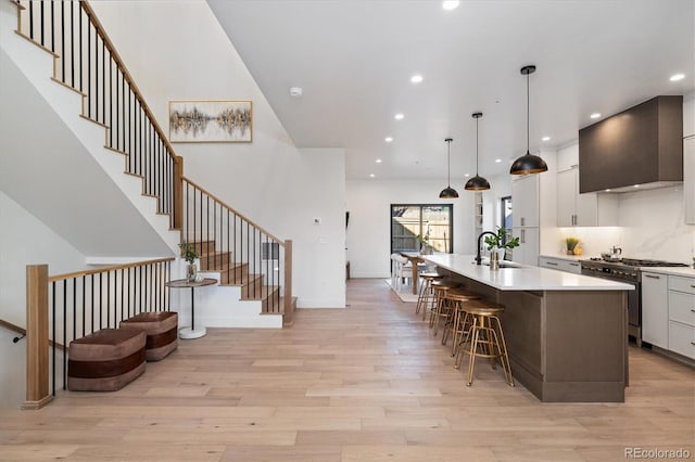 kitchen with a kitchen island with sink, stainless steel stove, pendant lighting, wall chimney exhaust hood, and white cabinets