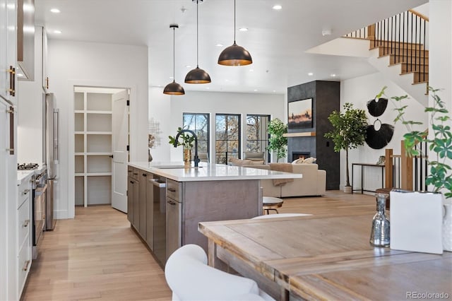 kitchen featuring hanging light fixtures, an island with sink, a fireplace, appliances with stainless steel finishes, and sink