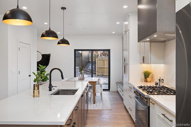 kitchen with appliances with stainless steel finishes, a large island with sink, wall chimney exhaust hood, white cabinets, and sink