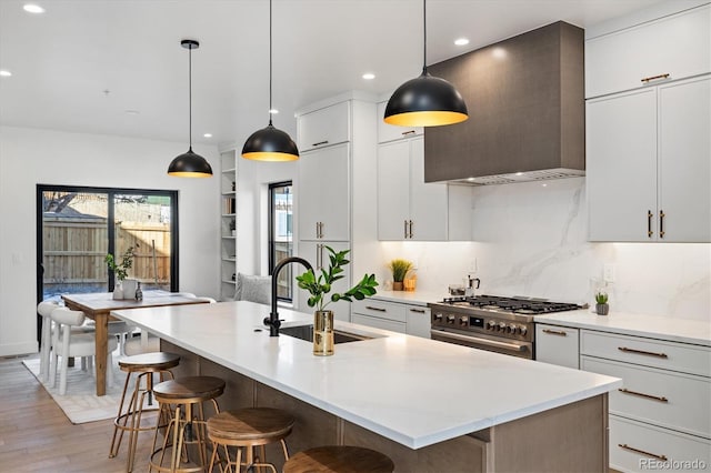 kitchen featuring sink, an island with sink, decorative light fixtures, and wall chimney exhaust hood