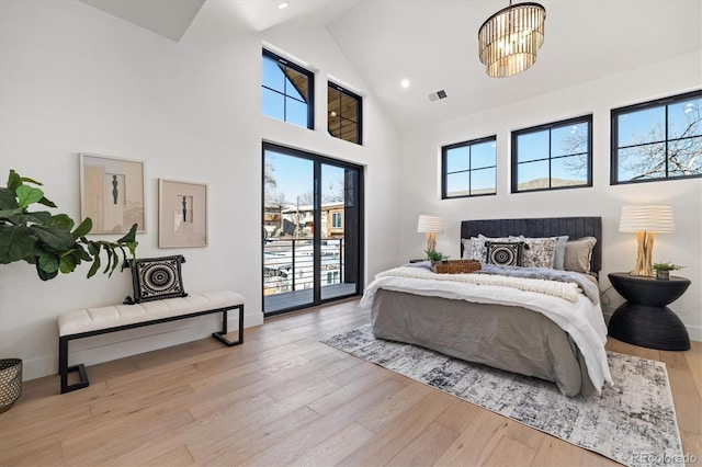 bedroom with a high ceiling, light hardwood / wood-style floors, access to outside, and an inviting chandelier