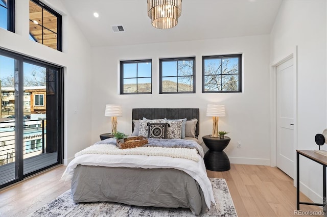 bedroom featuring access to outside, light wood-type flooring, a notable chandelier, and multiple windows