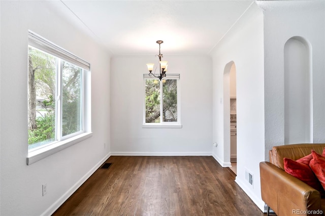 unfurnished dining area featuring arched walkways, dark wood-style flooring, a notable chandelier, and a healthy amount of sunlight