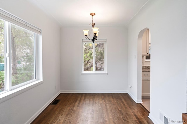 unfurnished dining area featuring visible vents, arched walkways, dark wood-style flooring, and a notable chandelier