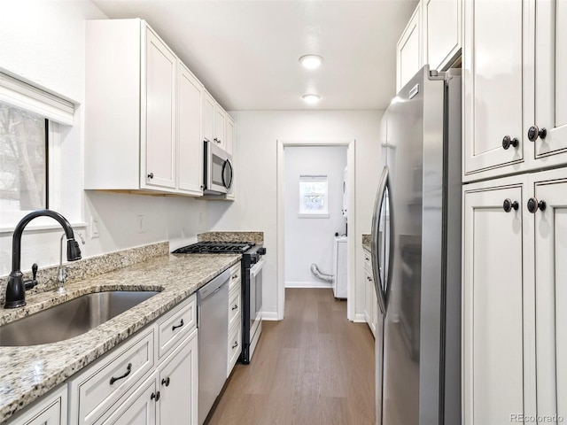 kitchen with white cabinets, light stone counters, appliances with stainless steel finishes, a sink, and wood finished floors