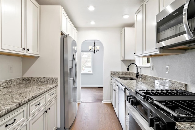 kitchen with a sink, a chandelier, light wood-style flooring, stainless steel appliances, and white cabinetry
