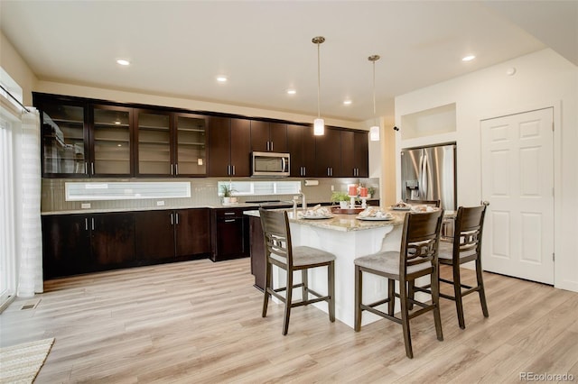4444 N Picadilly Ct, Aurora, CO 80019 - kitchen with stainless steel appliances, light wood finished floors, a breakfast bar, dark brown cabinets, and a kitchen island with sink