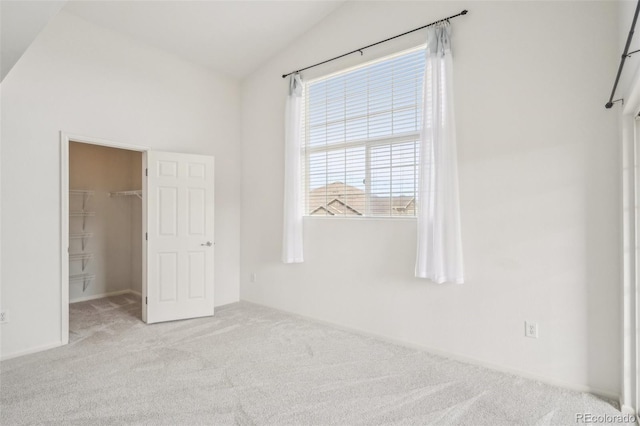 unfurnished bedroom featuring a walk in closet, vaulted ceiling, carpet flooring, and a closet