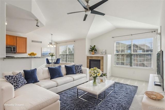 living area featuring a tiled fireplace, lofted ceiling, ceiling fan with notable chandelier, and visible vents