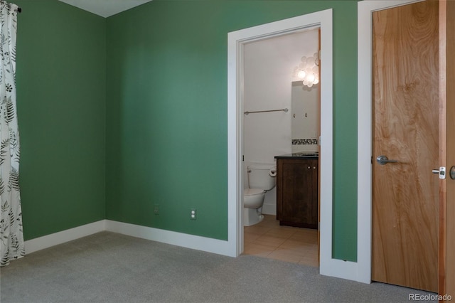 unfurnished bedroom featuring carpet flooring, baseboards, ensuite bathroom, and tile patterned flooring