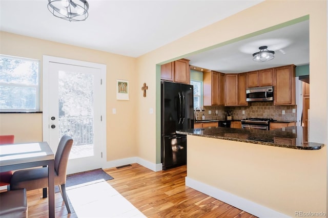 kitchen featuring tasteful backsplash, light wood-style flooring, dark stone countertops, brown cabinetry, and stainless steel appliances