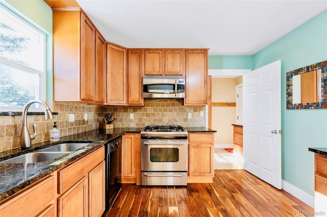 kitchen featuring tasteful backsplash, dark stone counters, appliances with stainless steel finishes, dark wood-style floors, and a sink