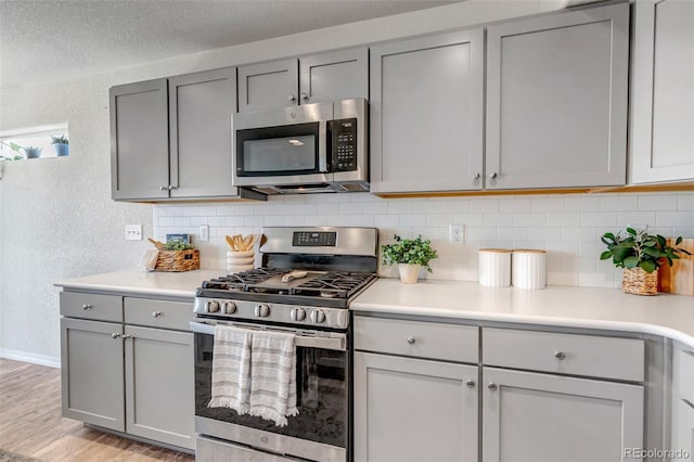 11051 Linley Way, Colorado Springs, CO 80908 - kitchen with stainless steel appliances, a textured wall, gray cabinetry, decorative backsplash, and light wood-type flooring