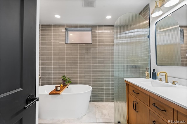 full bath featuring vanity, a soaking tub, recessed lighting, visible vents, and tile walls