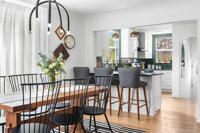 dining space featuring light wood finished floors and arched walkways