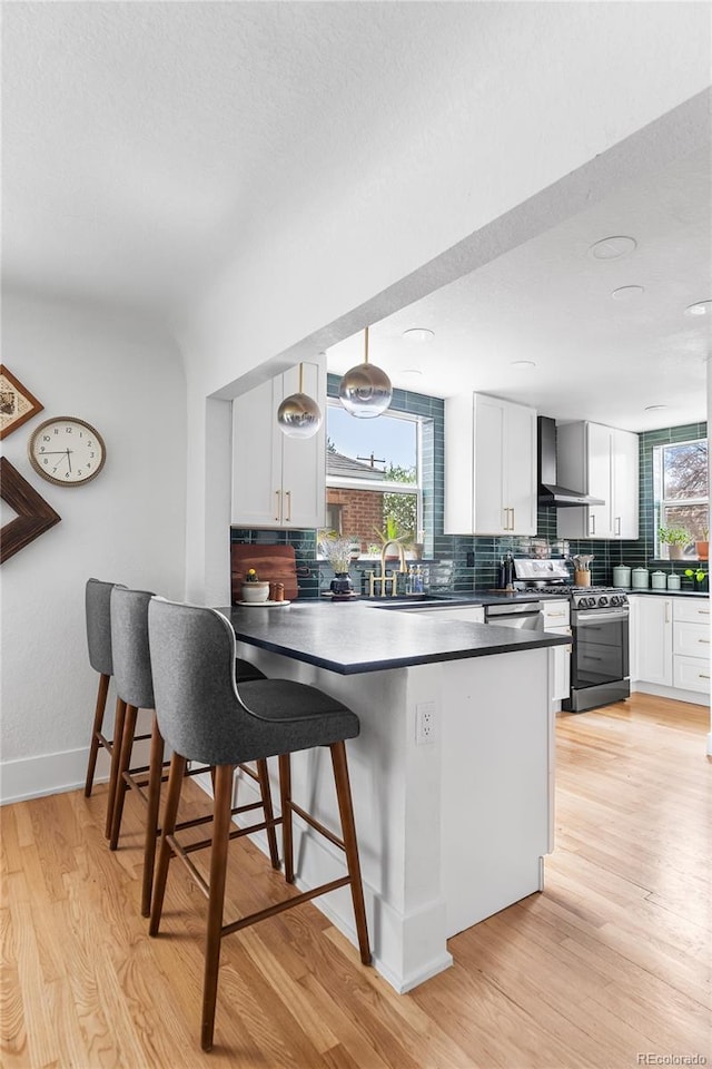 kitchen with wall chimney range hood, gas range, white cabinetry, and decorative backsplash
