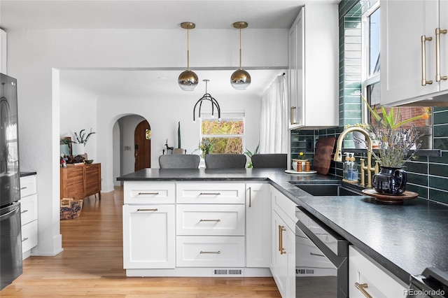 kitchen featuring visible vents, arched walkways, a sink, dark countertops, and dishwashing machine