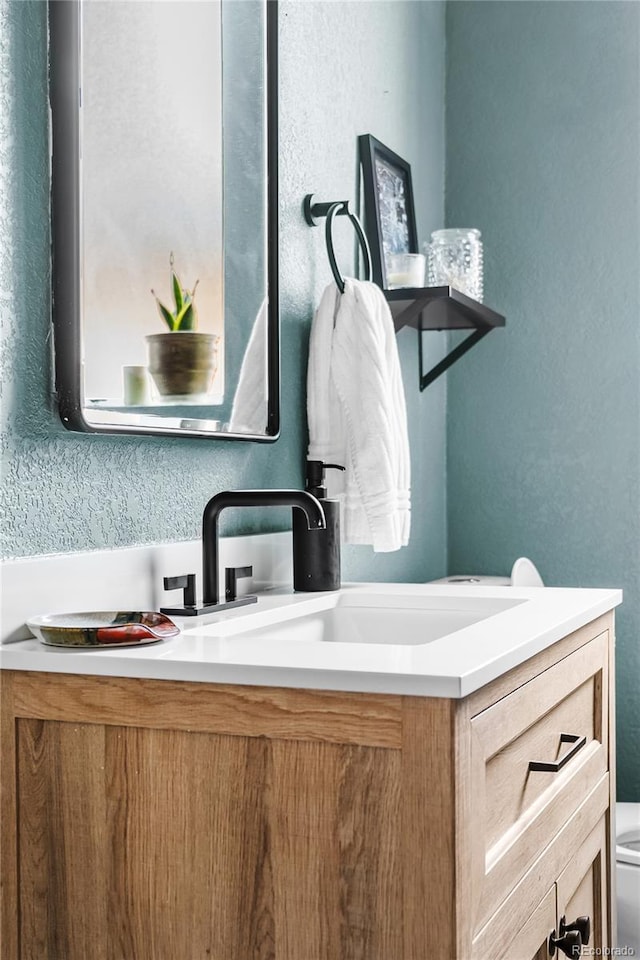 bathroom with a textured wall, vanity, and toilet