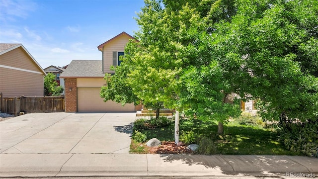 obstructed view of property featuring a garage, brick siding, driveway, and fence