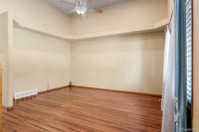 empty room with a ceiling fan, baseboards, visible vents, and wood finished floors