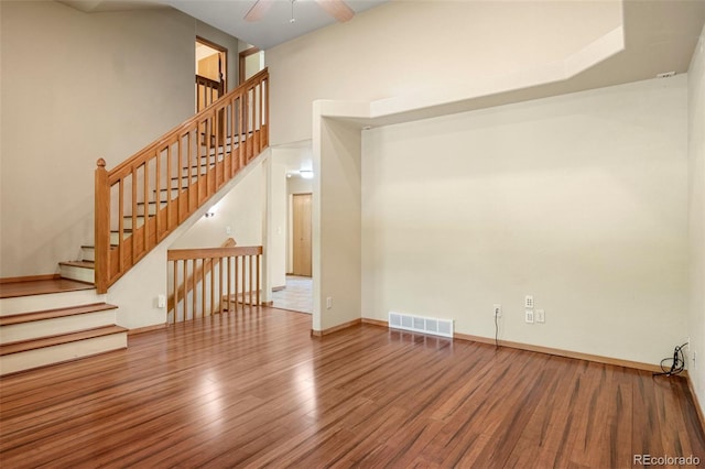 interior space featuring baseboards, visible vents, a ceiling fan, wood finished floors, and a high ceiling