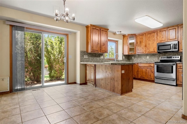 kitchen with tasteful backsplash, brown cabinetry, glass insert cabinets, a peninsula, and stainless steel appliances