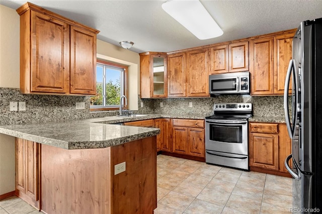 kitchen with stainless steel appliances, brown cabinetry, a peninsula, and a sink