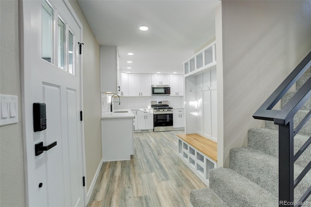 kitchen featuring stainless steel range with gas stovetop, backsplash, white cabinets, light hardwood / wood-style flooring, and sink