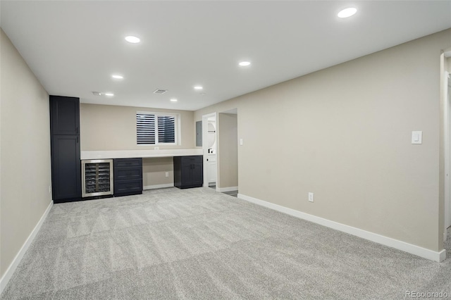 bar featuring light carpet, beverage cooler, and built in desk