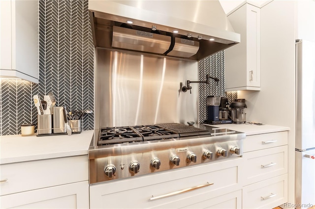 kitchen with white cabinets, stainless steel gas cooktop, light countertops, backsplash, and wall chimney exhaust hood