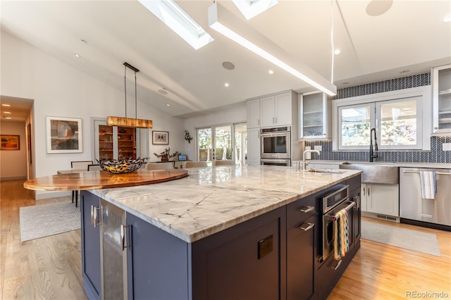kitchen featuring a large island with sink, stainless steel appliances, a sink, lofted ceiling with skylight, and light wood-style flooring