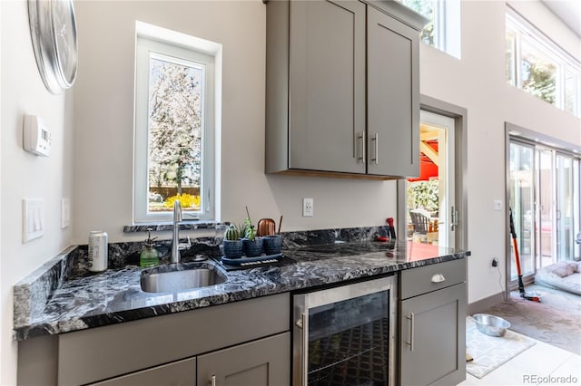 kitchen featuring gray cabinets, dark stone countertops, beverage cooler, and a sink
