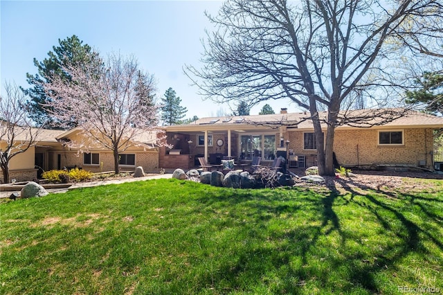 rear view of house with brick siding, a yard, and a patio