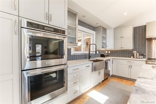 kitchen with light wood finished floors, a sink, tasteful backsplash, glass insert cabinets, and appliances with stainless steel finishes
