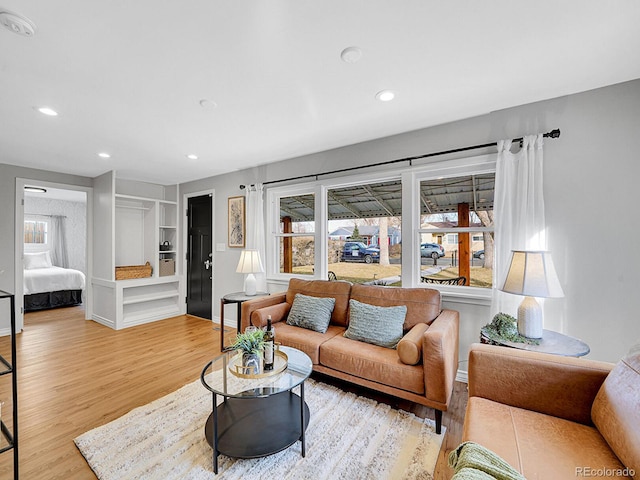 living room with built in shelves, recessed lighting, and light wood finished floors