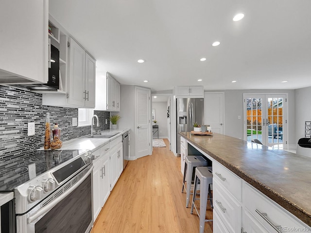 kitchen featuring stainless steel appliances, a sink, white cabinetry, light wood-type flooring, and decorative backsplash