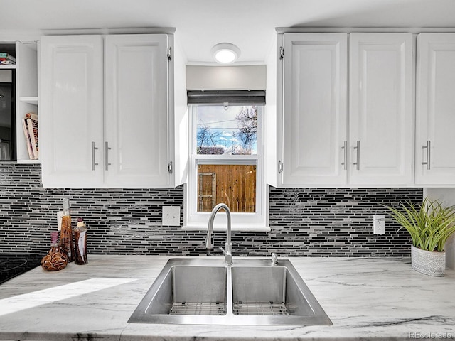 kitchen with white cabinetry, backsplash, a sink, and ornamental molding