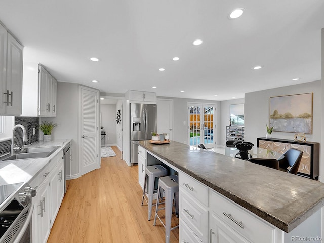 kitchen featuring a breakfast bar area, a sink, stainless steel appliances, light wood-type flooring, and backsplash