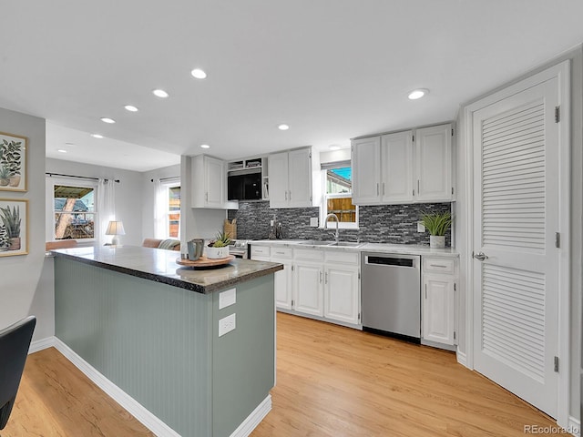 kitchen featuring light wood finished floors, decorative backsplash, stainless steel dishwasher, white cabinets, and a sink