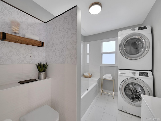 clothes washing area featuring laundry area, light tile patterned flooring, stacked washer and clothes dryer, and wallpapered walls