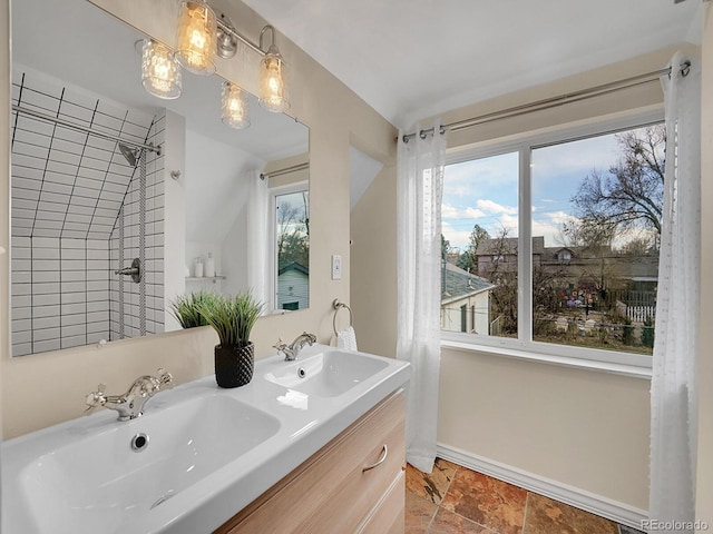 bathroom featuring double vanity, stone tile floors, baseboards, and a sink