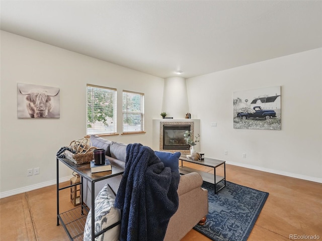 living area with a tiled fireplace, finished concrete flooring, and baseboards