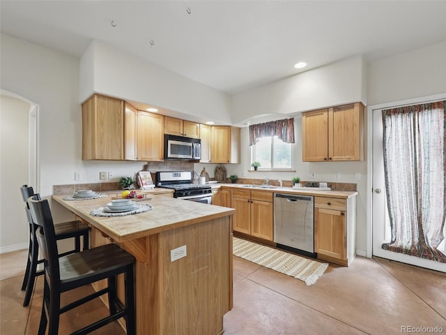 kitchen with stainless steel appliances, a kitchen bar, a sink, arched walkways, and a peninsula