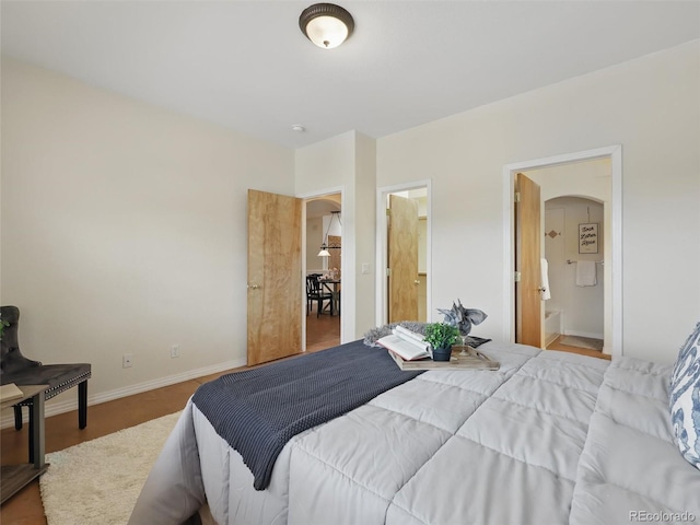 bedroom featuring arched walkways, connected bathroom, and baseboards